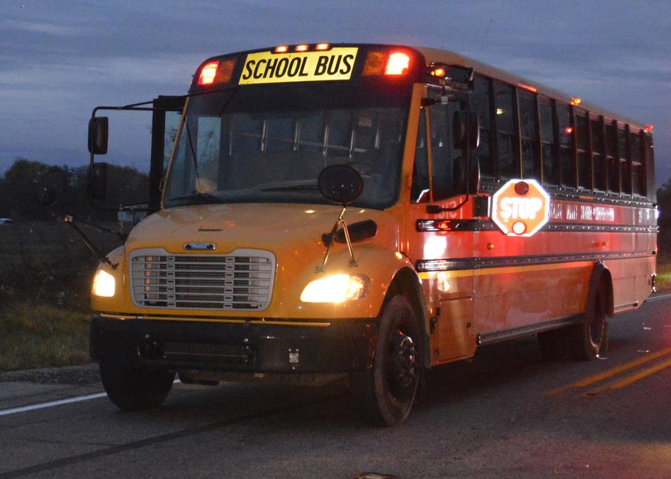 A school bus at dusk, red lights flashing and stop arm out
