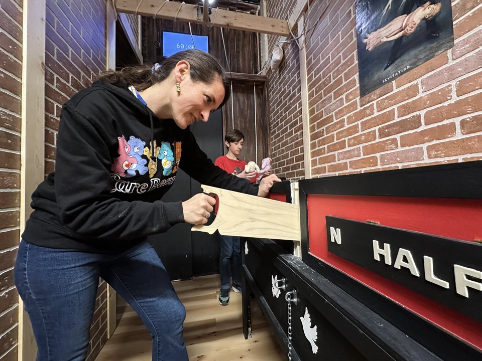 A player works the sawing-box puzzle with a wooden saw in the brick-walled room