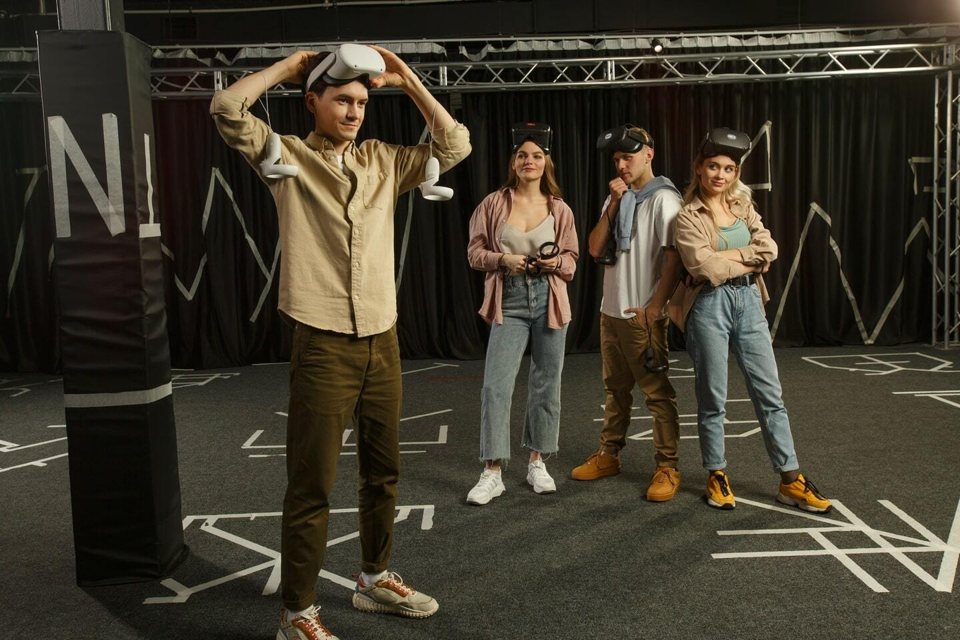 Four players with VR headsets and controllers in the black-curtained play arena