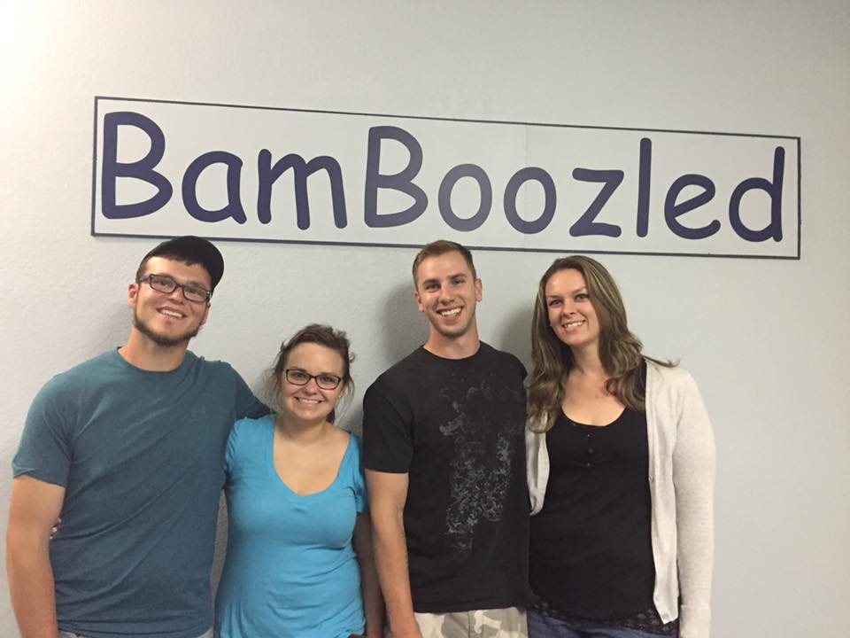 A team of four smiles in front of the BamBoozled sign