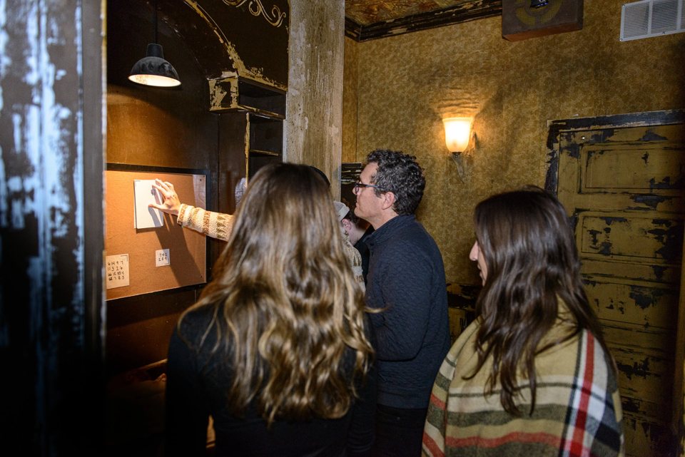 Players study clues on a corkboard in a worn, lamp-lit room
