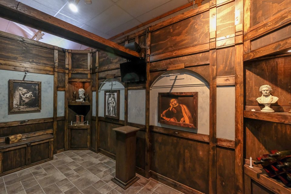 Wood-paneled gallery room with framed paintings, marble busts and a pedestal in the middle