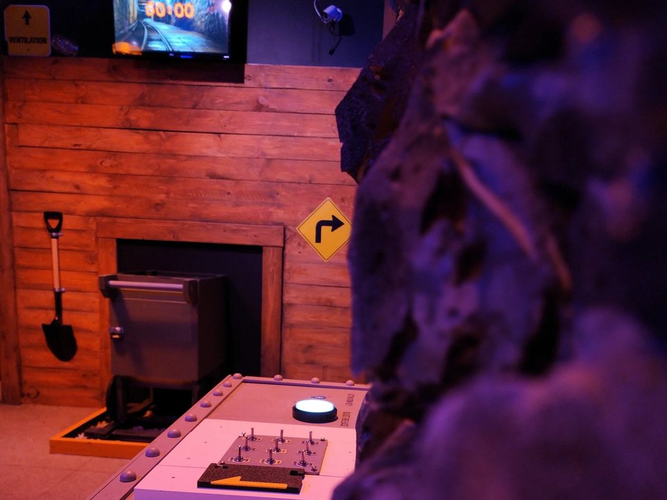 Mine-themed room with rough rock walls, wooden planks, an ore cart and a control panel below a countdown screen