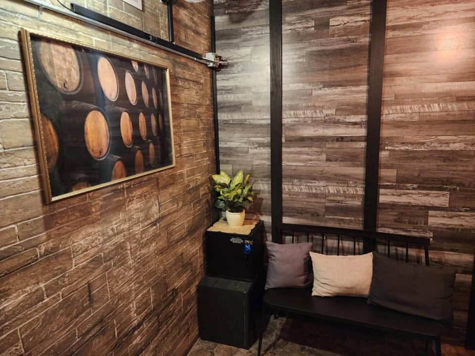 Lobby corner with a bench, cushions, a potted plant and a wine barrel picture on the brick wall