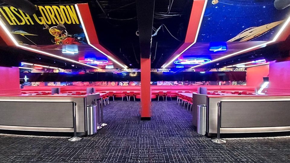 A szórakoztatóközpont neonfényes pihenőtere piros bokszokkal, székekkel és Flash Gordon-képregényes falfestményekkel