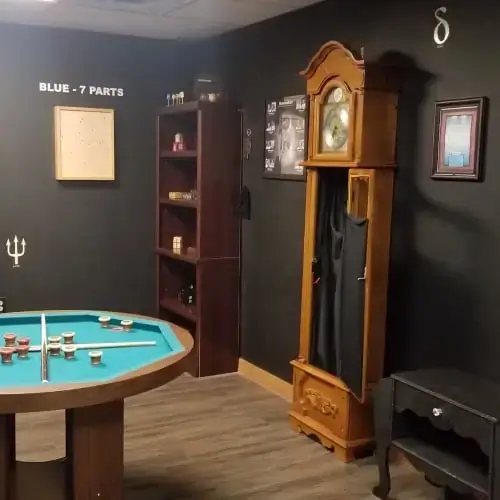 Dark gray room with a round game table, a bookcase and a tall grandfather clock