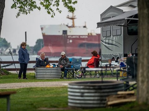Campers by a fire ring with a freighter passing behind them