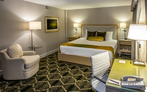 A guest room with a king bed, an armchair and a desk