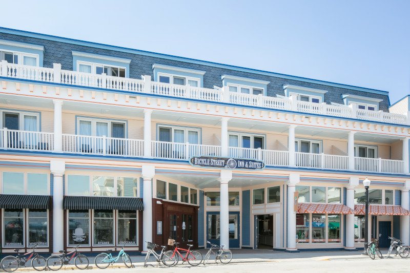 A szálloda fehér, erkélyes homlokzata a Bicycle Street Inn & Suites felirattal és a bejárat előtt álló biciklikkel