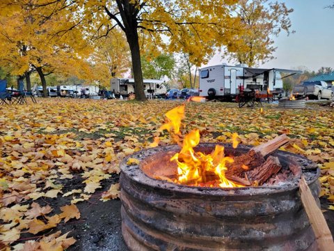 A campfire among autumn leaves with campers behind