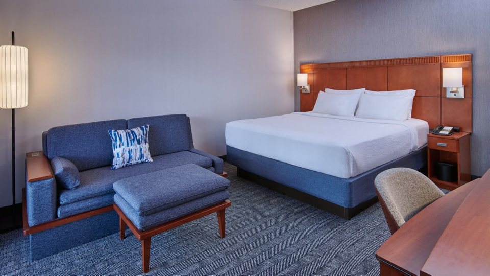 A guest room with a king bed, a blue sofa and a desk