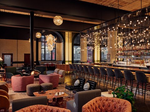 The hotel bar and lounge with hanging string lights, a long bar counter and pink armchairs