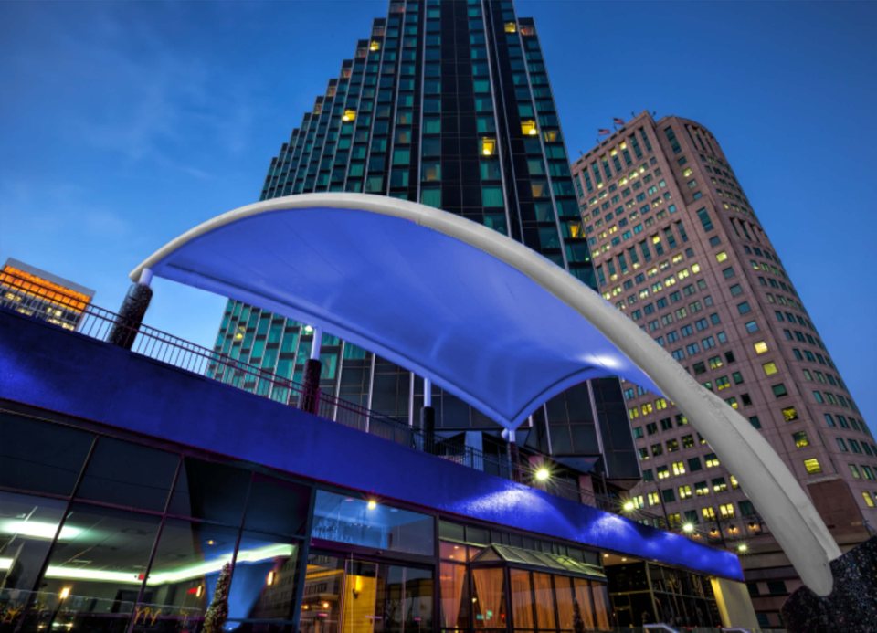 The hotel tower and its curved entrance canopy seen from below, lit up in the evening
