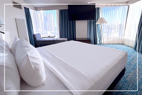 A guest room with a large bed and windows overlooking the city