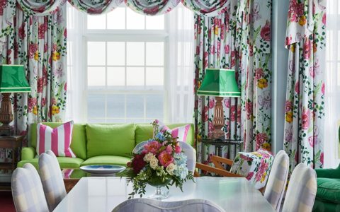 A suite with floral curtains, a green sofa and a window overlooking the lake