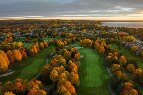 The resort's golf course with autumn trees from above, with the bay in the background