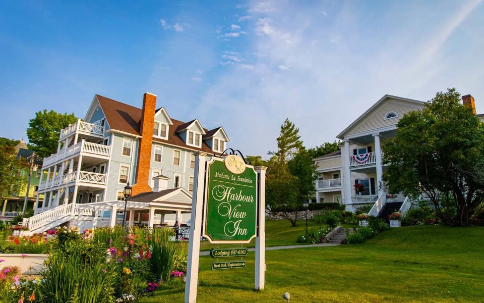 The green Harbour View Inn sign in front of the blue and white wooden houses in a flower garden