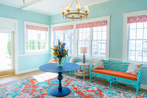 A bright turquoise sitting room with a round table, a chandelier and a colorful rug