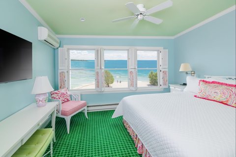 A guest room with light blue walls, a green carpet and windows looking out on the lake