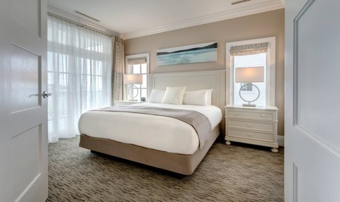A bright guest room with a king bed and sheer-curtained balcony doors
