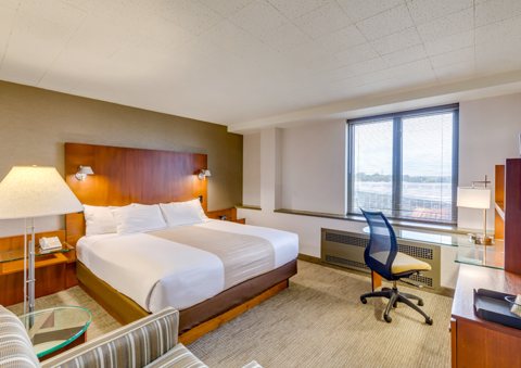 A guest room with a king bed, a desk and a large window