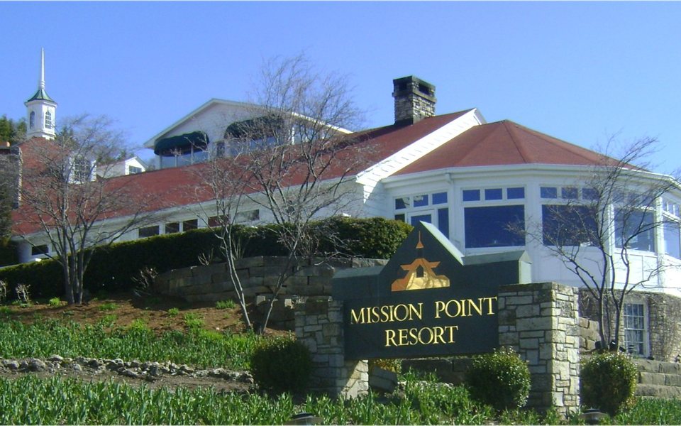 The Mission Point Resort's white, red-roofed main lodge and its stone-framed entrance sign under a blue sky