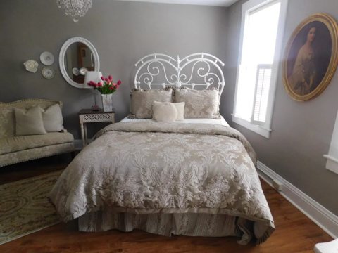 A gray-walled guest room with a white wrought-iron headboard, a settee and an old portrait on the wall