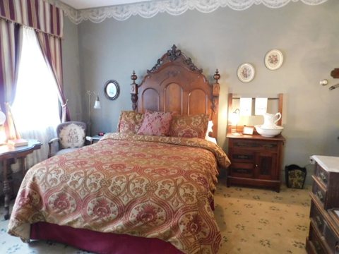 A guest room with a tall carved Victorian wooden bed, a patterned bedspread and striped curtains
