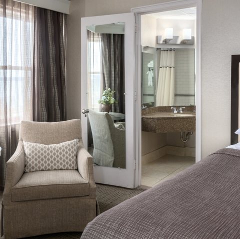 A guest room with an armchair by the window and an open door to the bathroom