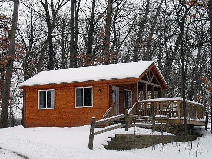 A wooden cabin with a snow-covered porch in the woods