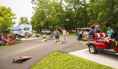A campground lane with a cornhole game and a golf cart