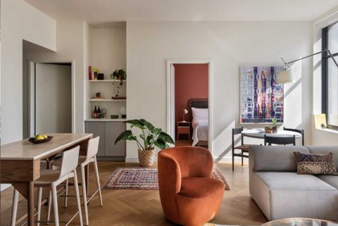 Napfényes apartman-nappali konyhapulttal, narancssárga fotellel és a hálószobába nyíló ajtóval