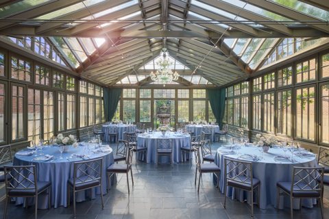 A glass-roofed conservatory with round set tables at the hotel