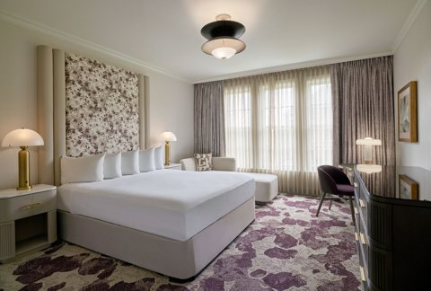 A guest room with a king bed, floral wallpaper and a writing desk