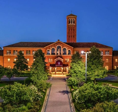 The lit main entrance and bell tower at dusk, with a garden walkway in front