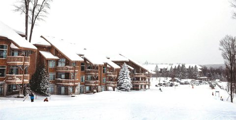 Wood-clad lodging buildings with balconies beside a snowy ski slope