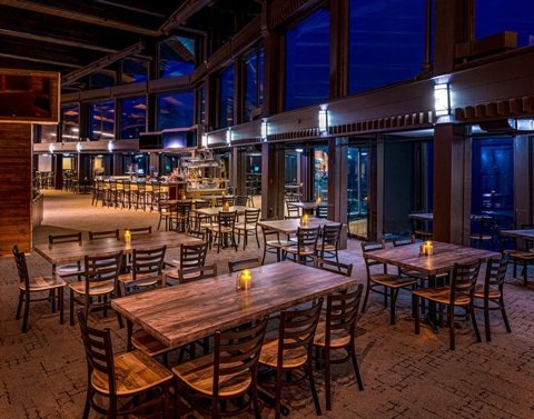 The long wooden tables of the glass-walled restaurant in evening light