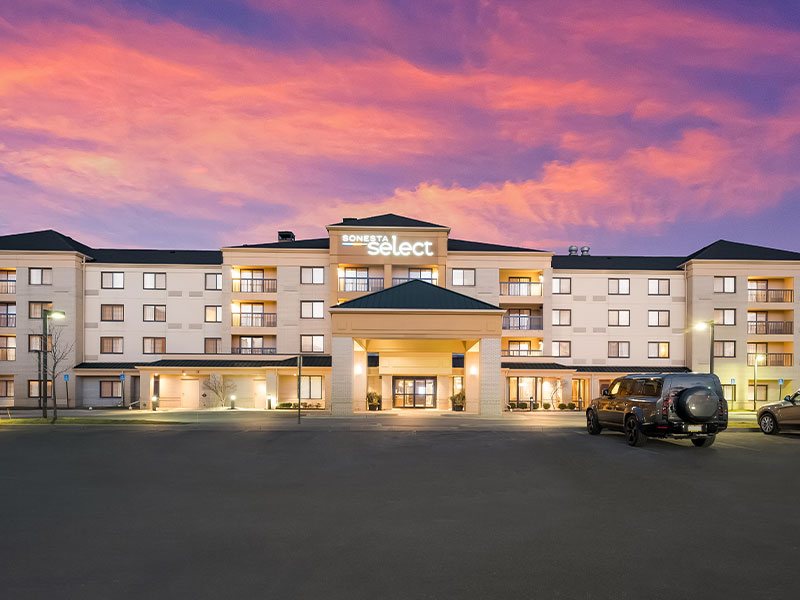 The hotel's lit facade with the Sonesta Select sign under a pink evening sky