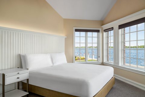 A bright guest room with a queen bed and windows facing the river