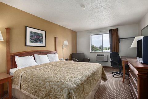 A guest room with a queen bed, a desk and a television