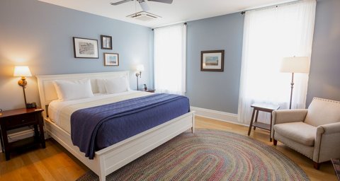 A guest room with a queen bed, a braided rug and an armchair