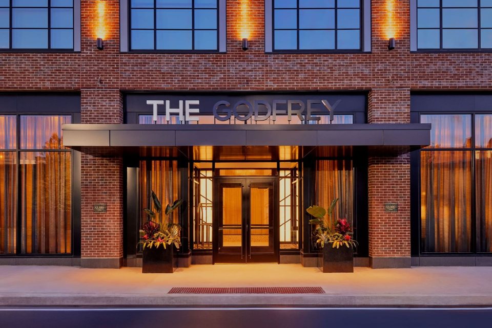 The Godfrey's brick facade with its name and lit glass entrance at dusk