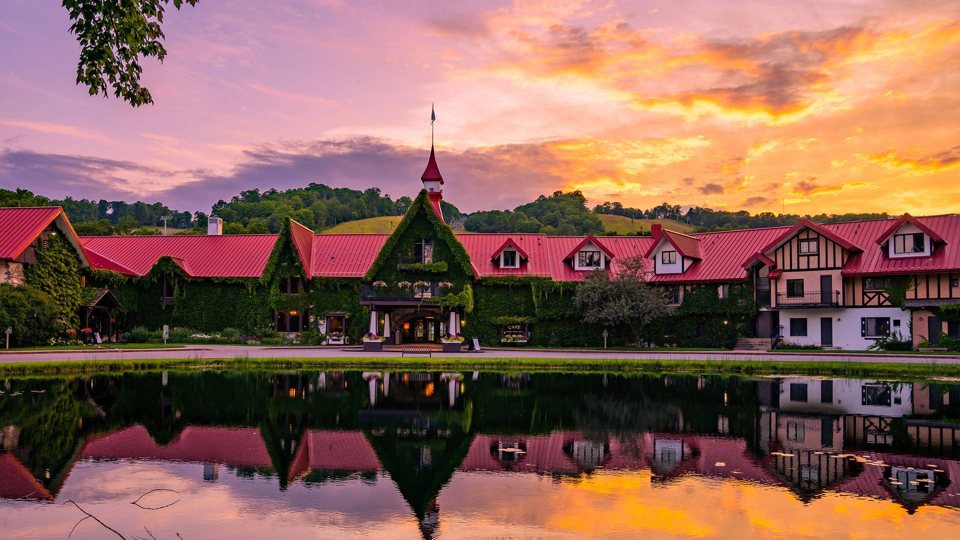 The main lodge's red roofs and tower reflected in the pond at sunset