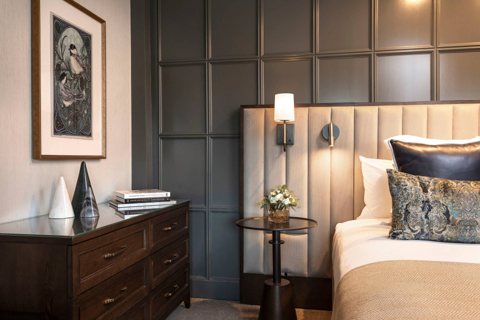 A guest room with an upholstered headboard, a dresser and a wall lamp
