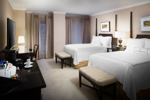 Guest room with two beds in white linens, benches and a desk