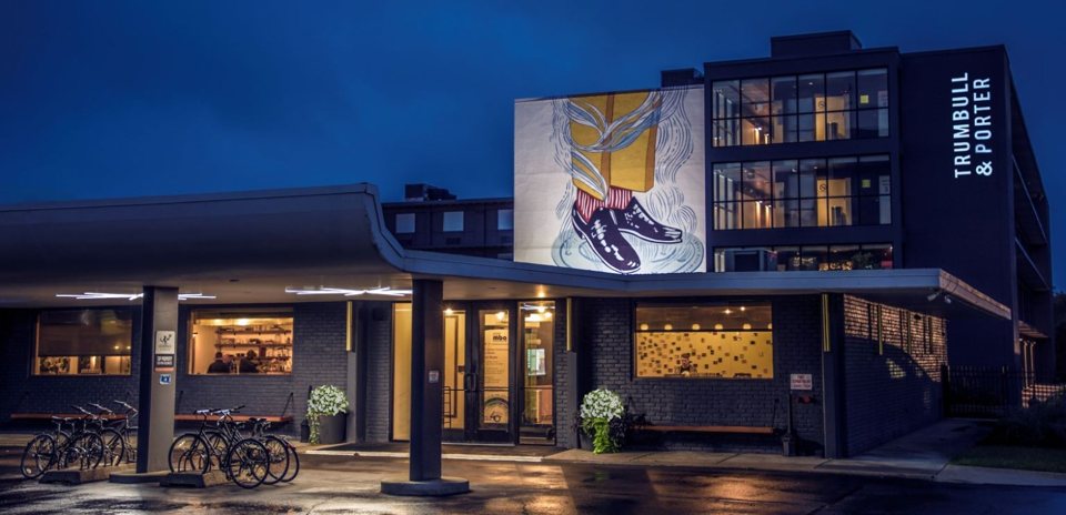 The hotel building at night with a large mural and a vertical name sign on the facade