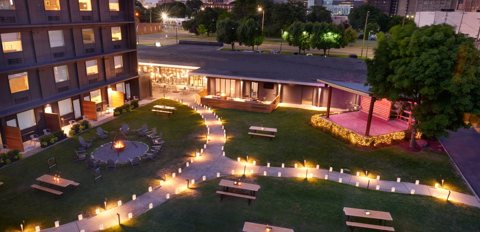 The hotel courtyard at night with string lights, a fire pit and picnic tables