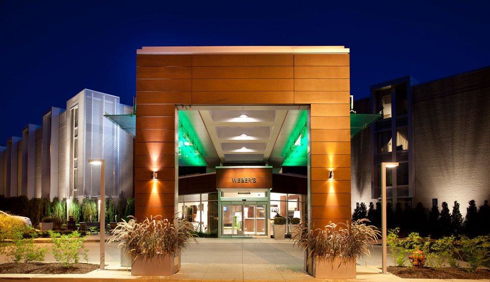 The hotel's lit entrance at night with a wood-clad portal and planters