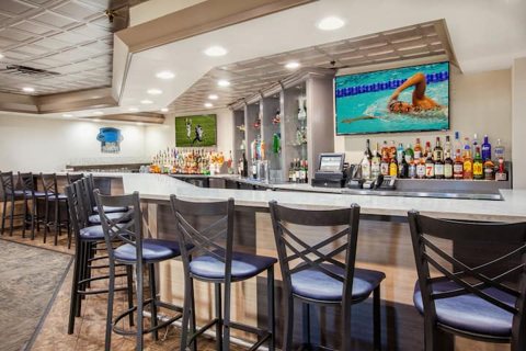 The hotel bar with bar stools, shelves of bottles and TVs