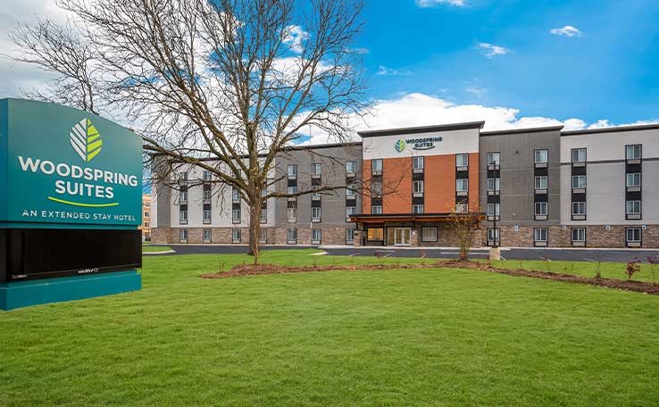 A szálloda négyszintes épülete a WoodSpring Suites táblával és a gyepes előkerttel
